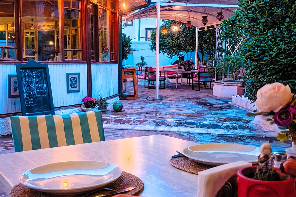 restaurant-outdoors Charming outdoor restaurant setting with a table for two in the foreground, surrounded by colorful chairs, hanging lanterns, and lush greenery under soft evening lights.